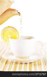 Hot tea being poured from a teapot into a cup with lemon