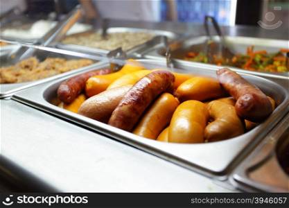 Hot tray with thick sausages close-up in dining room