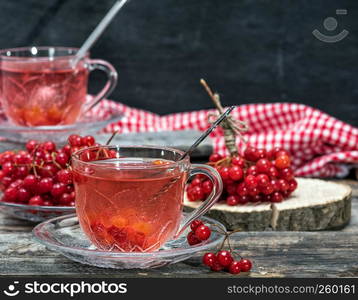 hot viburnum tea in a transparent cup with a handle and saucer on a gray wooden table