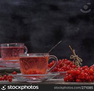 hot viburnum tea in a transparent cup with a handle and saucer on a gray wooden table, next to fresh berries
