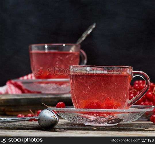 hot viburnum tea in a transparent cup with a handle and saucer on a gray wooden table