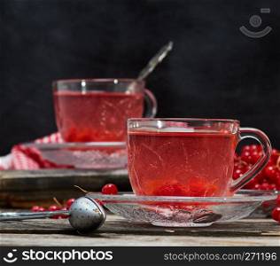 hot viburnum tea in a transparent cup with a handle and saucer on a gray wooden table