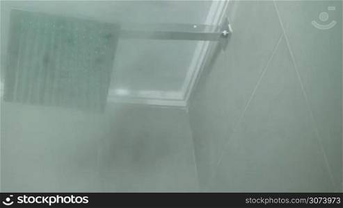Hot water is flowing from the modern square shower head. Steam is appearing on the camera.