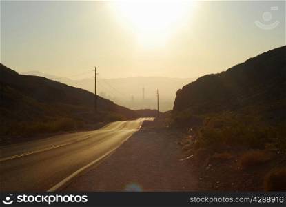 Hot wavy asphalt road leading into hazy Las Vegas against sun.