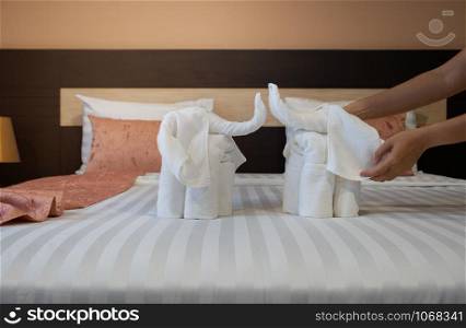 Hotel maid cleaning bedroom service. Close-up of hands folding white bath towels like elephant on the bed sheet.