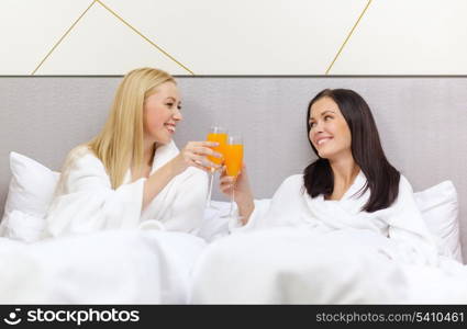 hotel, travel, friendship and happiness concept - smiling girlfriends having breakfast in bed