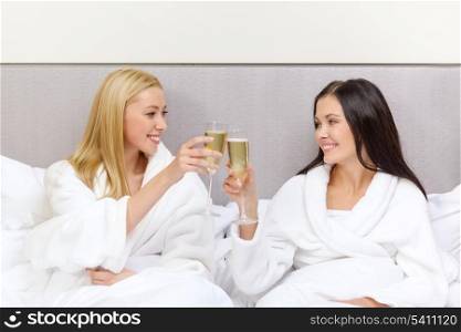 hotel, travel, friendship and happiness concept - smiling girlfriends with champagne glasses in bed