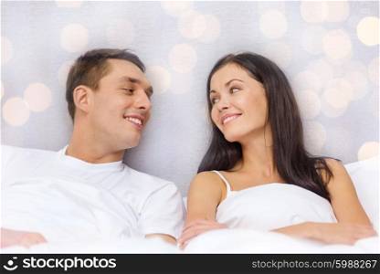 hotel, travel, relationships, and happiness concept - happy couple dreaming in bed over lights background