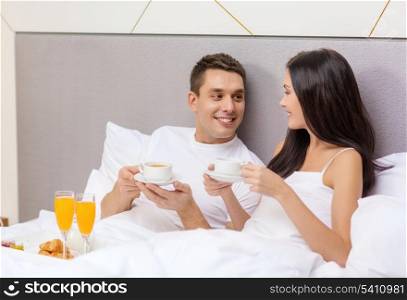hotel, travel, relationships and happiness concept - smiling couple having breakfast in bed in hotel room