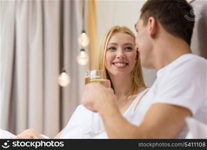 hotel, travel, relationships and happiness concept - smiling couple with champagne glasses in bed