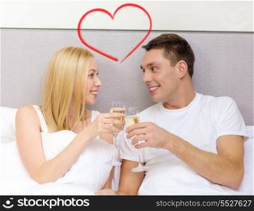 hotel, travel, relationships and happiness concept - smiling couple with champagne glasses in bed