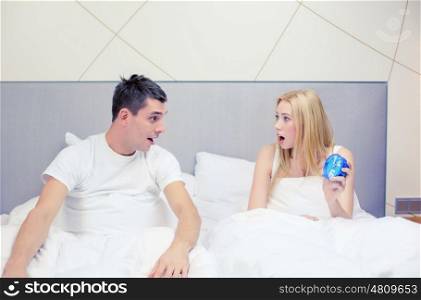 hotel, travel, relationships and happiness concept - surprised couple with clock in bed