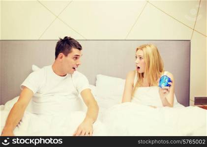 hotel, travel, relationships and happiness concept - surprised couple with clock in bed