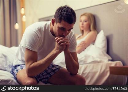 hotel, travel, relationships, and sexual problems concept - upset man sitting on the bed with woman on the back
