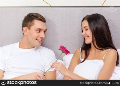 hotel, travel, relationships, holidays and happiness concept - smiling couple in bed with pink flower