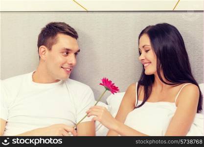 hotel, travel, relationships, holidays and happiness concept - smiling couple in bed with pink flower