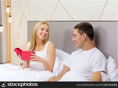 hotel, travel, relationships, holidays and happiness concept - smiling couple in bed with red gift box