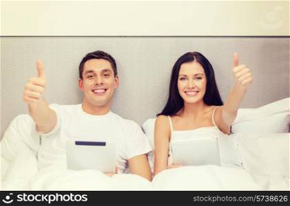 hotel, travel, relationships, technology, intermet and happiness concept - smiling couple in bed with tablet computers showing thumbs up