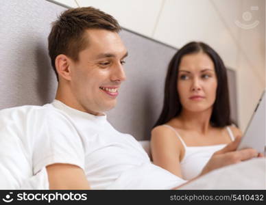 hotel, travel, relationships, technology, intermet and happiness concept - smiling couple in bed with tablet computer