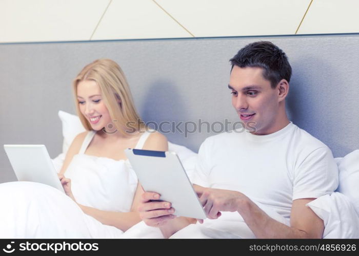 hotel, travel, relationships, technology, intermet and happiness concept - smiling couple in bed with tablet computers