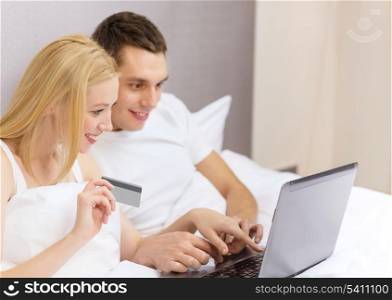 hotel, travel, relationships, technology, internet and happiness concept - smiling couple in bed with laptop and credit card