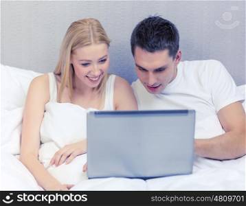 hotel, travel, relationships, technology, internet and happiness concept - smiling couple in bed with laptop