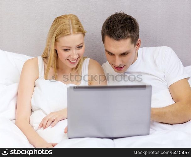 hotel, travel, relationships, technology, internet and happiness concept - smiling couple in bed with laptop