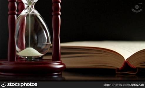 hourglass and book on black background.