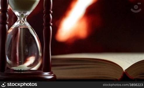 hourglass and book on the background of burning fireplace.