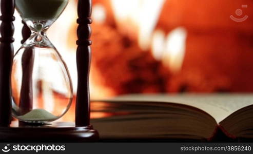 hourglass and book on the background of burning fireplace.