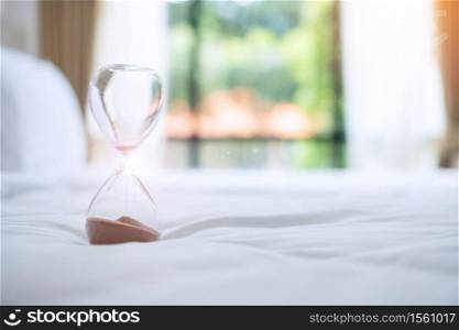 Hourglass on bed in the morning sunlight, Sand flowing through the bulb of Sandglass measuring the passing time. countdown, deadline, Life time and Retirement, daily routine concept