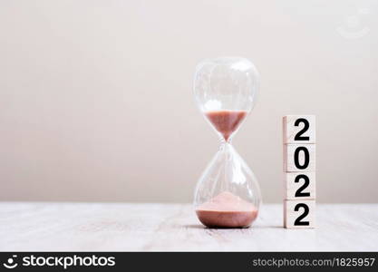 Hourglass with 2022 wooden cube blocks on table, Sand flowing through the bulb of Sandglass measuring the passing time. countdown, deadline, Happy New Year, Resolution and New Start concept