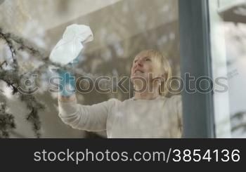 House chores with elderly woman cleaning window glass at home. Tilt shot