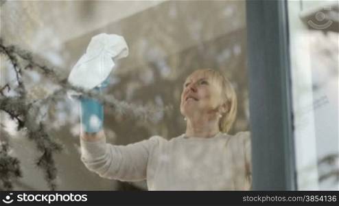 House chores with elderly woman cleaning window glass at home. Tilt shot