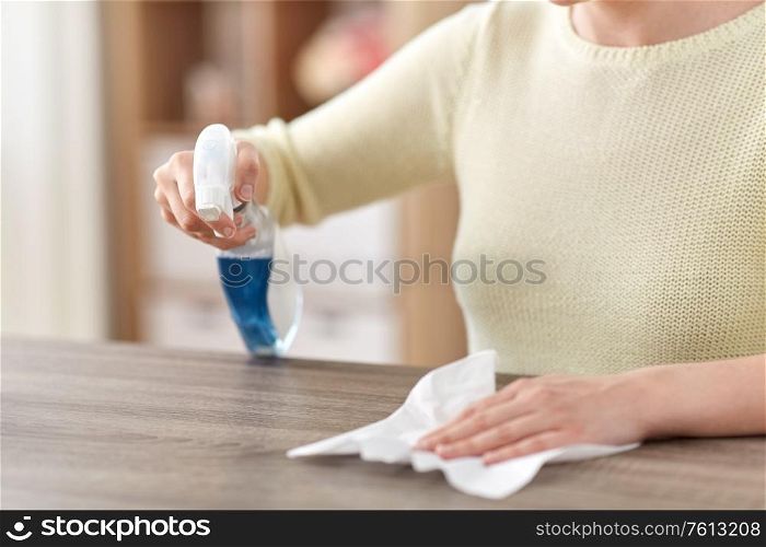house cleaning, hygiene and disinfection concept - close up of woman or housewife with spray detergent and paper tissue wiping table at home. close up of woman cleaning table at home
