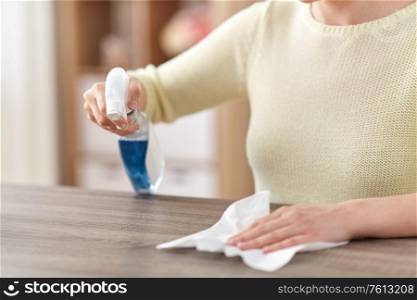 house cleaning, hygiene and disinfection concept - close up of woman or housewife with spray detergent and paper tissue wiping table at home. close up of woman cleaning table at home