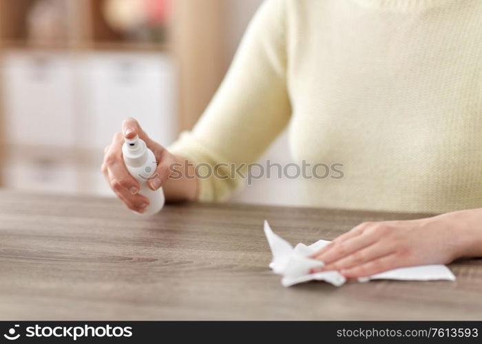 house cleaning, hygiene and disinfection concept - close up of woman or housewife with spray sanitizer and paper tissue wiping table at home. close up of woman cleaning table at home