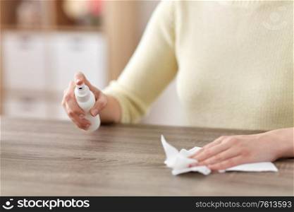 house cleaning, hygiene and disinfection concept - close up of woman or housewife with spray sanitizer and paper tissue wiping table at home. close up of woman cleaning table at home