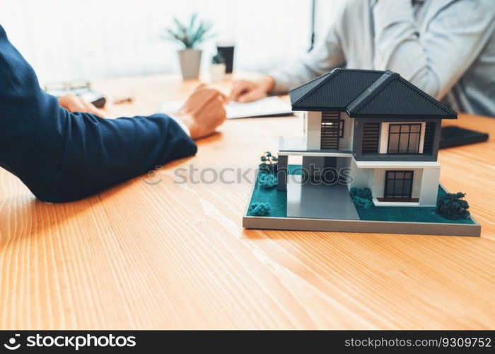 House model is displayed on wooden meeting table with in the blurred background of real estate agent and client discuss terms and conditions of house loan or rental lease contract. Entity. House model is displayed on wooden meeting table with blur background. Entity