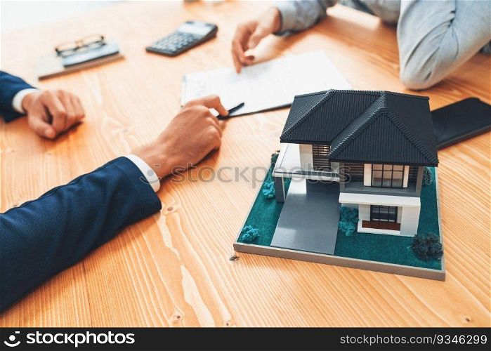 House model is displayed on wooden meeting table with in the blurred background of real estate agent and client discuss terms and conditions of house loan or rental lease contract. Entity. House model is displayed on wooden meeting table with blur background. Entity