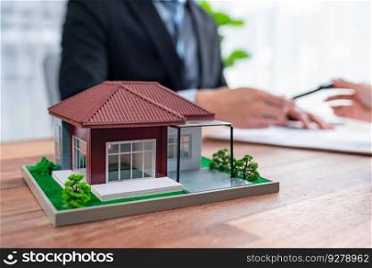 House model sample on wooden table with blurred background of real estate agent and buyer or client discussing terms and condition on house loan contract. Housing business meeting. Jubilant. House model sample on wooden table with blurred background. Jubilant