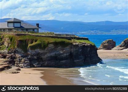 House on cliff and summer Atlantic sandy beach Los Castros (Galicia, Spain).