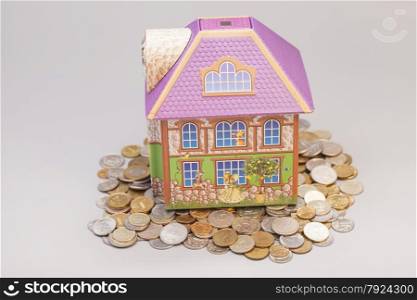 House standing on heap of coins on gray.Real estate concept