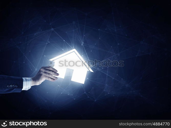 House symbol in hand. Hand of businessman on dark background showing glowing house sign