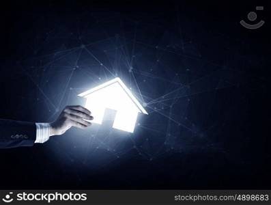 House symbol in hand. Hand of businessman on dark background showing glowing house sign