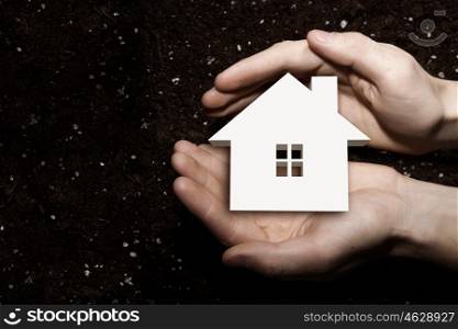 House symbol in palms. Male hands holding house sign in palms on soil background