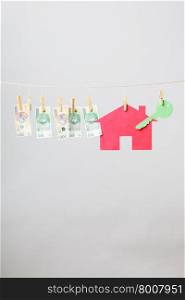 House with key and banknotes. Red house with green key and banknotes cash hang on laundry line on grey background. Selling and buying home concept.