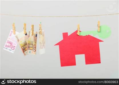 House with key and banknotes. Red house with green key and banknotes cash hang on laundry line on grey background. Selling and buying home concept.