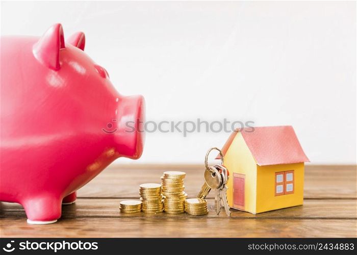 house with key stacked coins besides piggybank