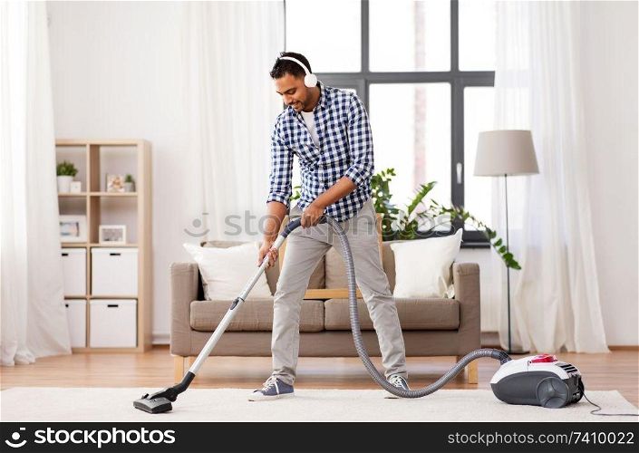 household and cleaning concept - indian man in headphones with vacuum cleaner at home. man in headphones with vacuum cleaner at home